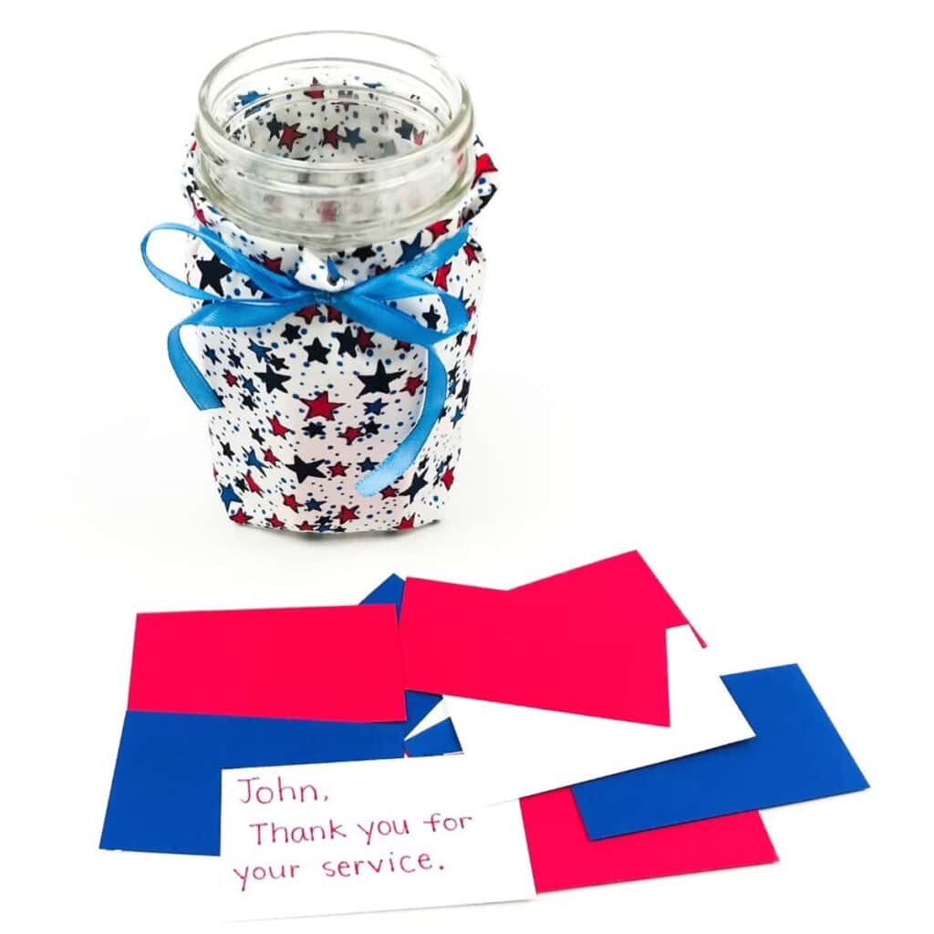 mason jar covered in red and blue star fabric with a blue bow and red white and blue slips of paper with notes of gratitude written on them for Memorial Day activities for kids 