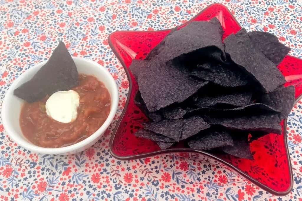 blue corn tortillas in a red star serving tray, red salsa with white sour cream on top sitting on a patriotic tablecloth